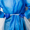A close-up of a person wearing a blue disposable protective gown and blue gloves, pulling a white plastic barrier away from the torso.